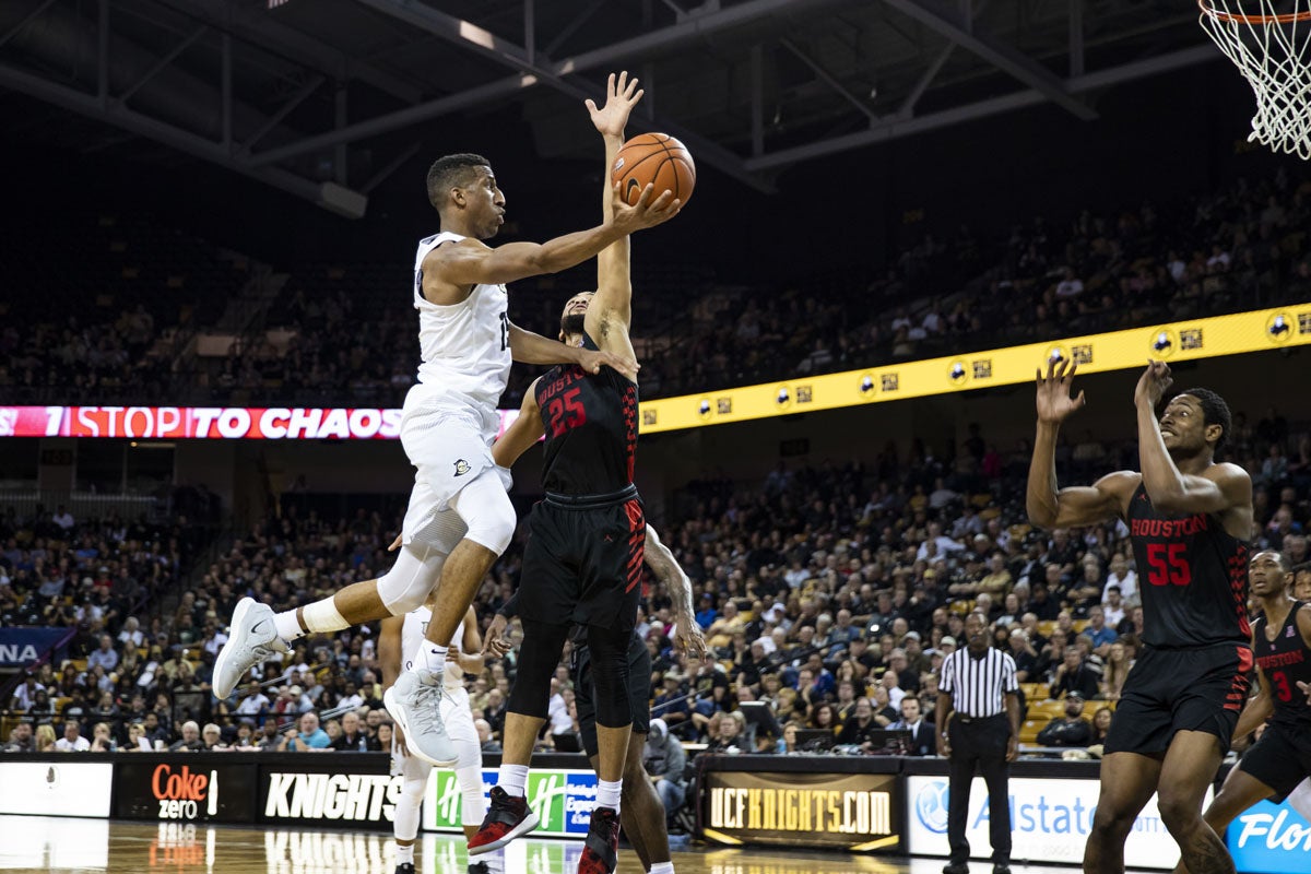 A UCF basketball player jumps to make a shot while a player from the opposing team tries to stop him.