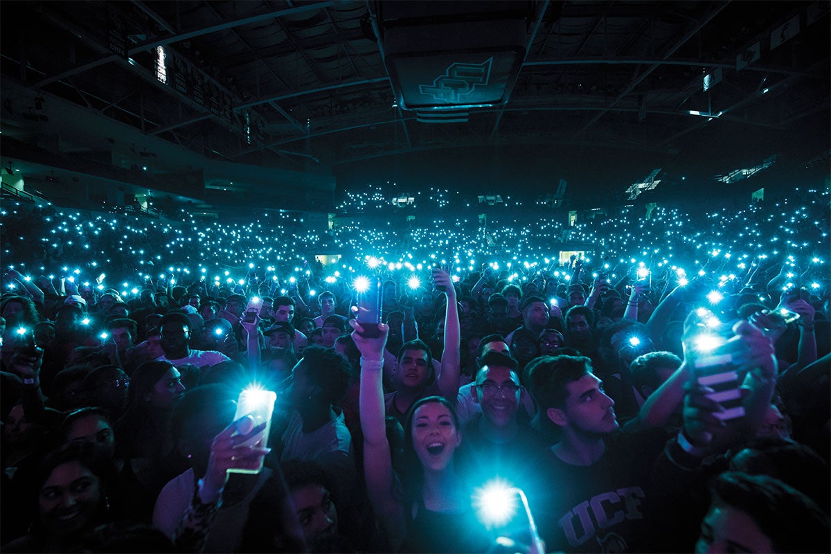A crowd of students hold up their cellphones with their flashlights on at a concert.