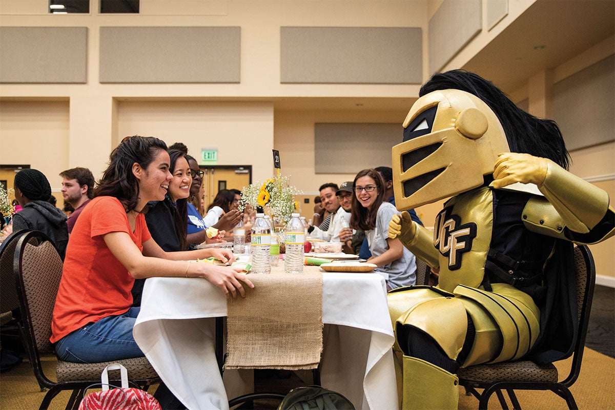 Knightro sits at a banquet table with students.