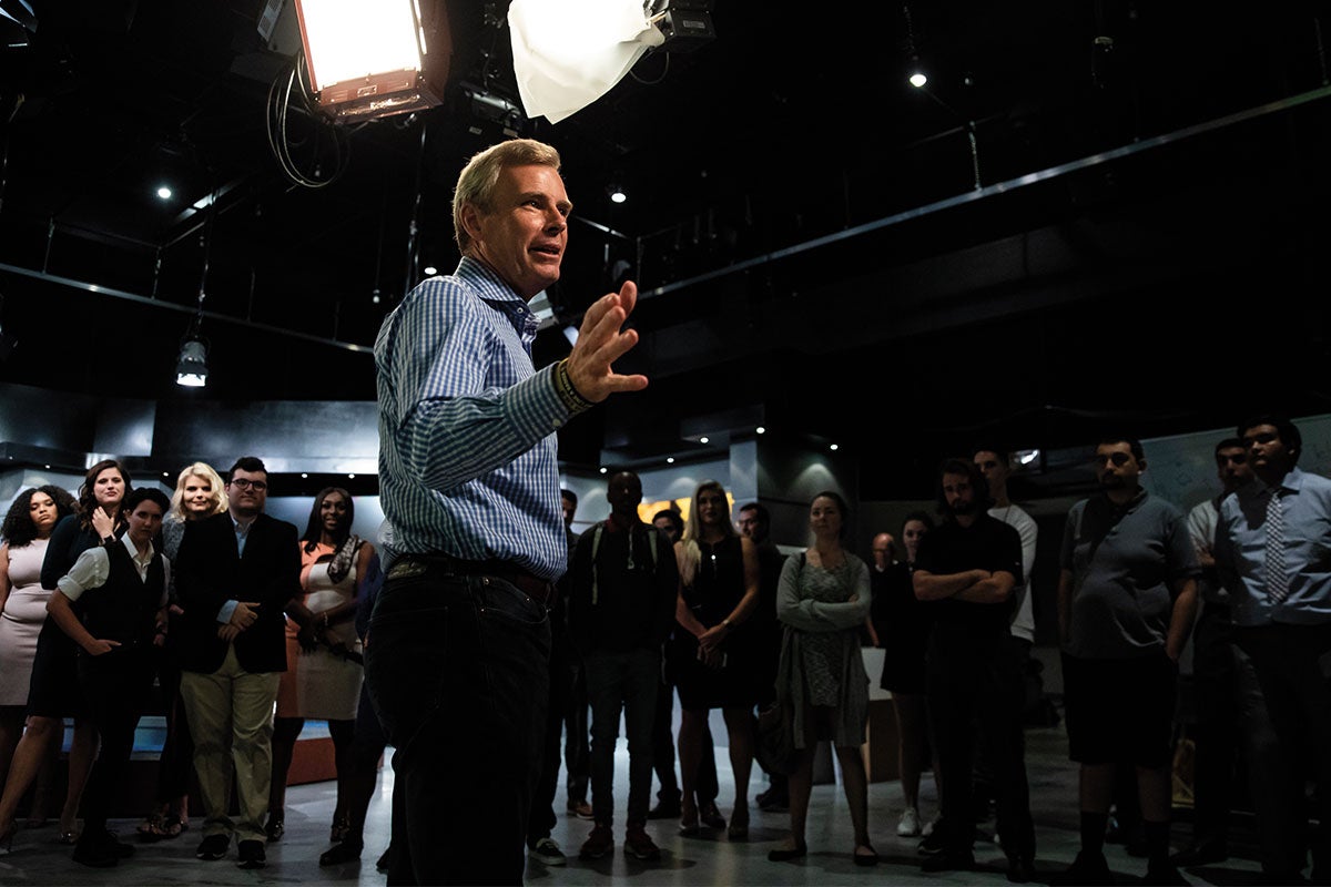 Tom Rinaldi speaks to a group of students in a dark studio.