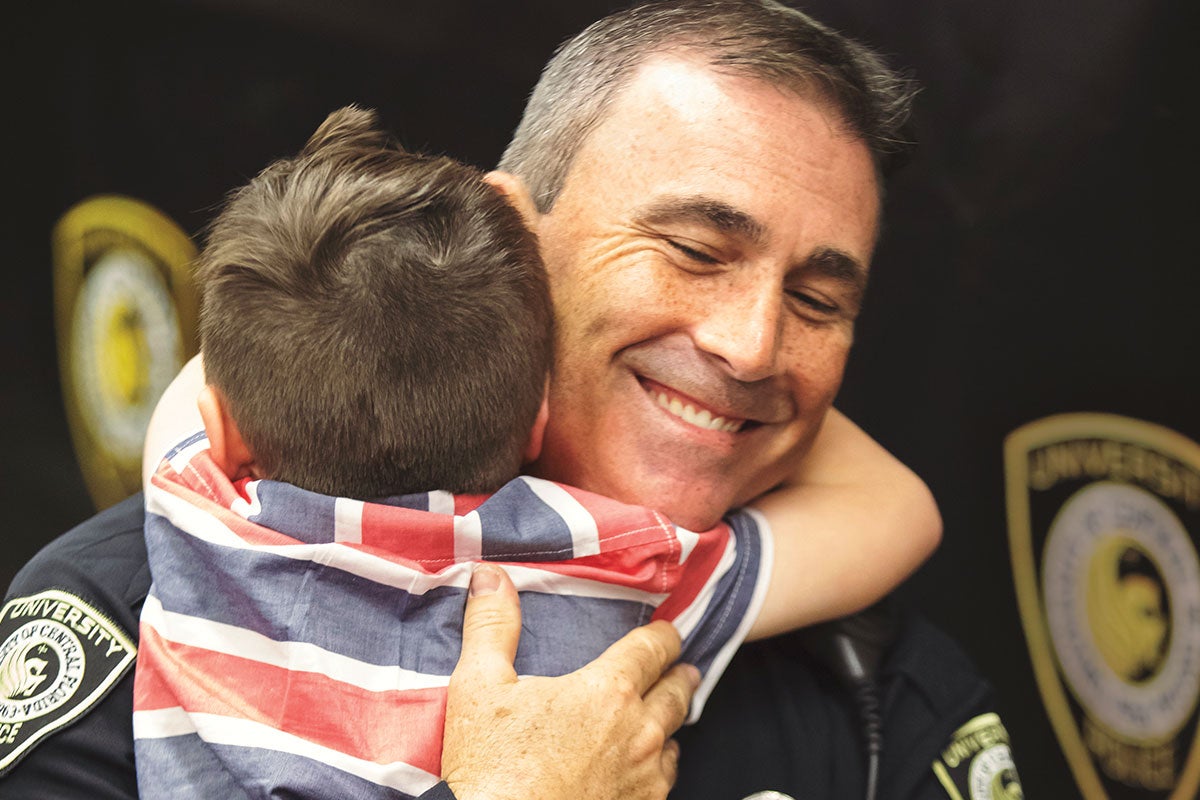 A police officer in uniform hugs a young boy.