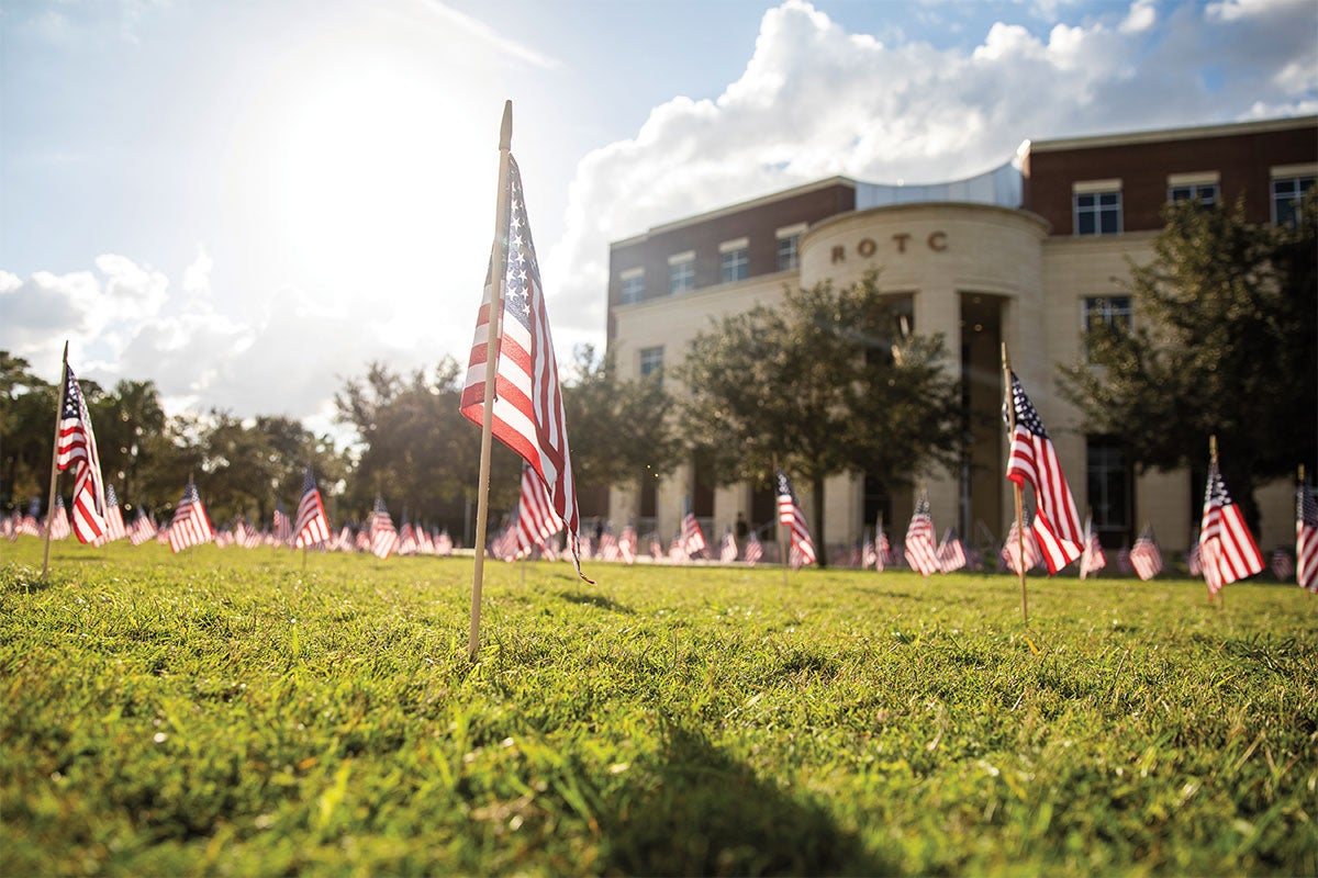 Small American flags decorate a green lawn outside the ROTC building.