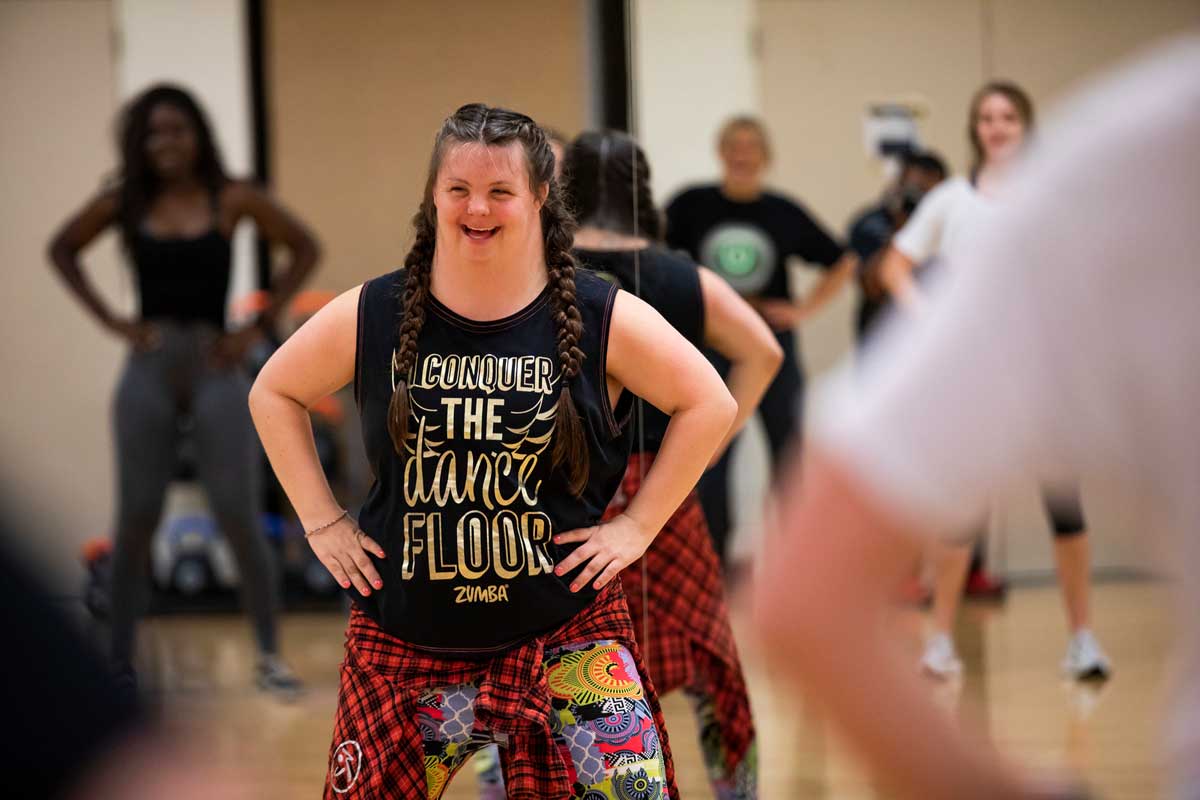 UCF student stands with hands on hips in front of exercise class