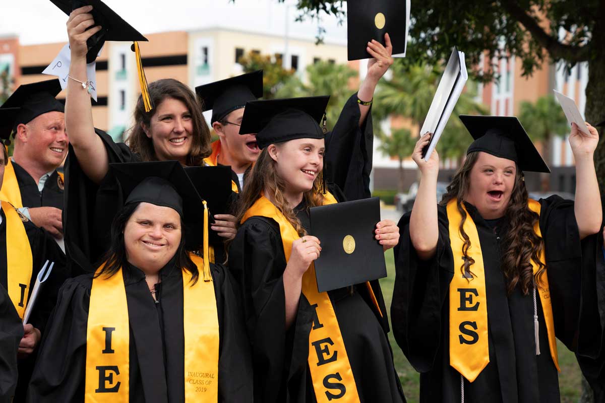 Group of graduates celebrate with arms and diplomas raised in the air