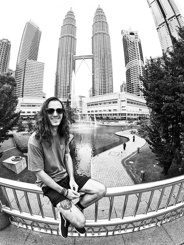 A black and white photo of a man sitting in front of tall buildings.