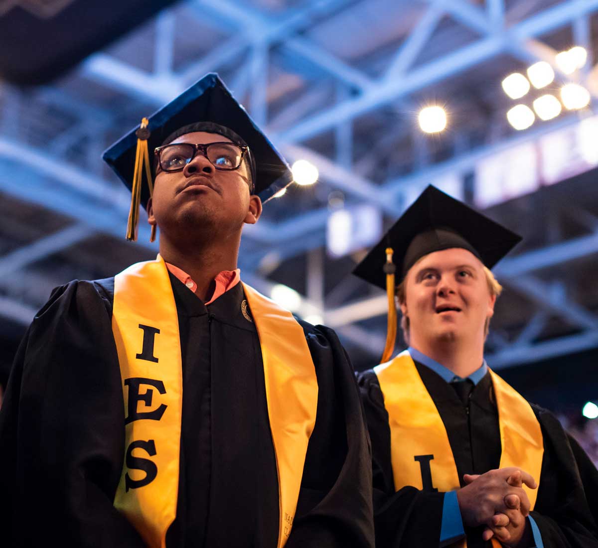 Two male graduates stand side by side in their caps and gowns