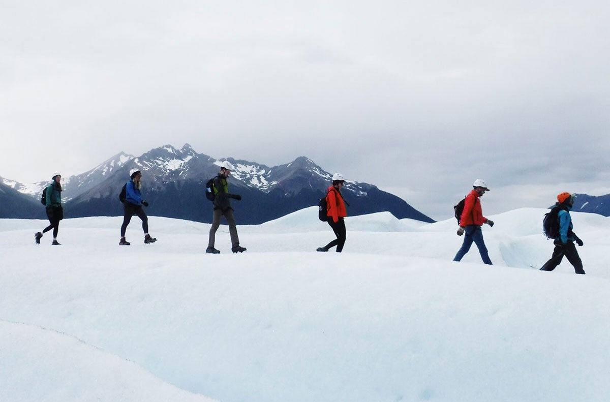 A group of people walking across ice while in front of mountains.