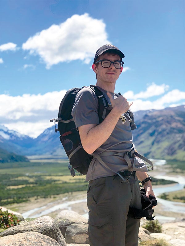 A man with a backpack posing in front of a mountain.