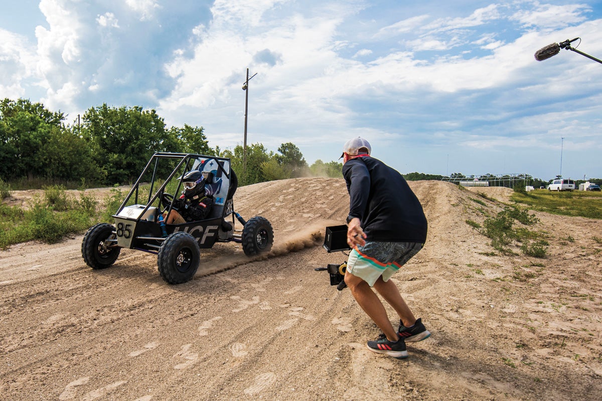 A cameraman records someone driving a baja vehicle.