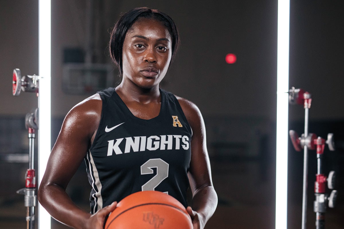 A female basketball player holds a ball while wearing a Knights jersey.