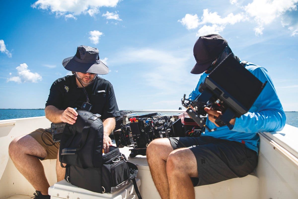 Two cameramen set up their equipment in a boat.