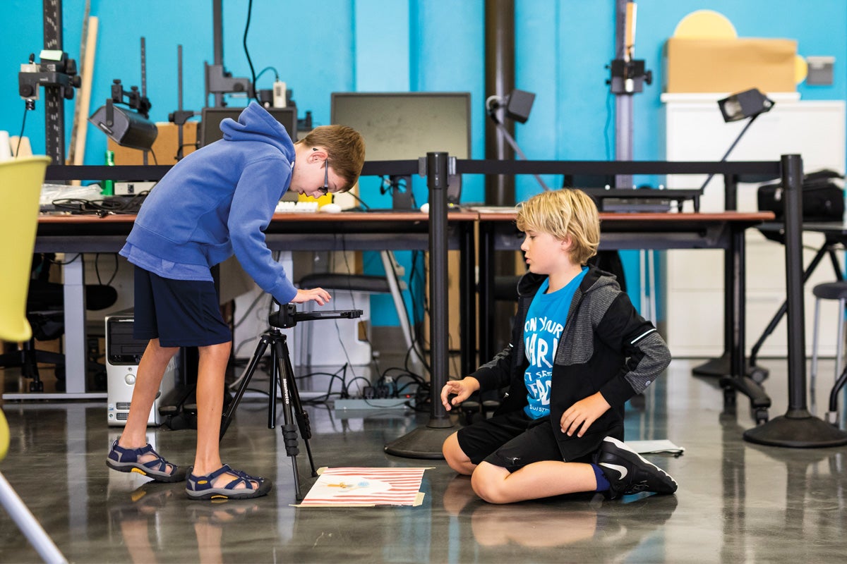 Two kids take a picture of a drawing.