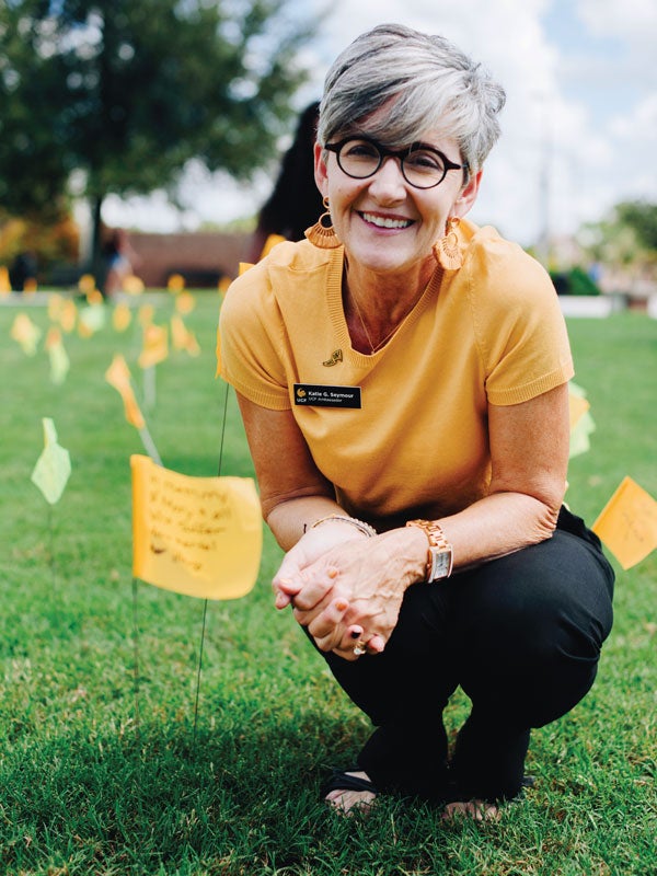 Katie Seymour smiles while crouching in a field of yellow flags with messages on them. UCF Fall 2019