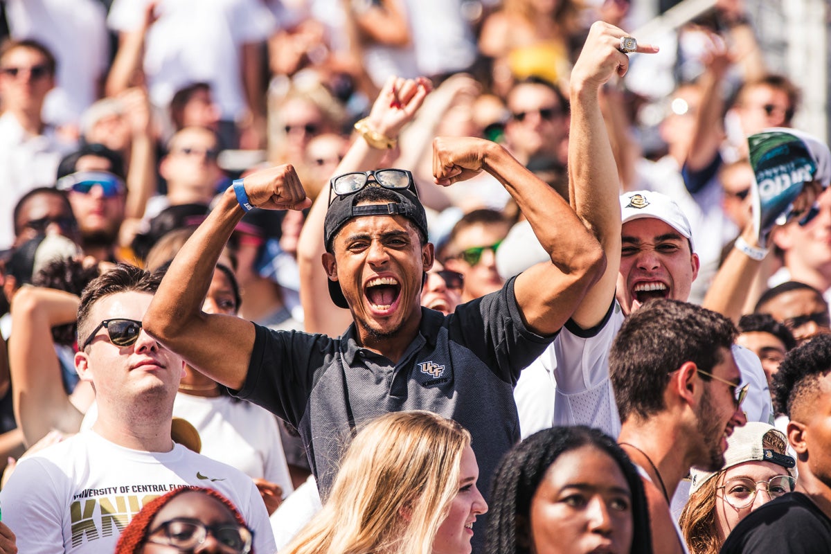 One fan smiles and raises his arms within a sea of fans. UCF Fall 2019
