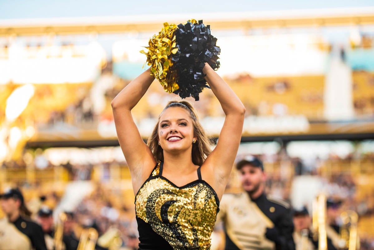 A dancer holds pompoms over her head while she smiles.