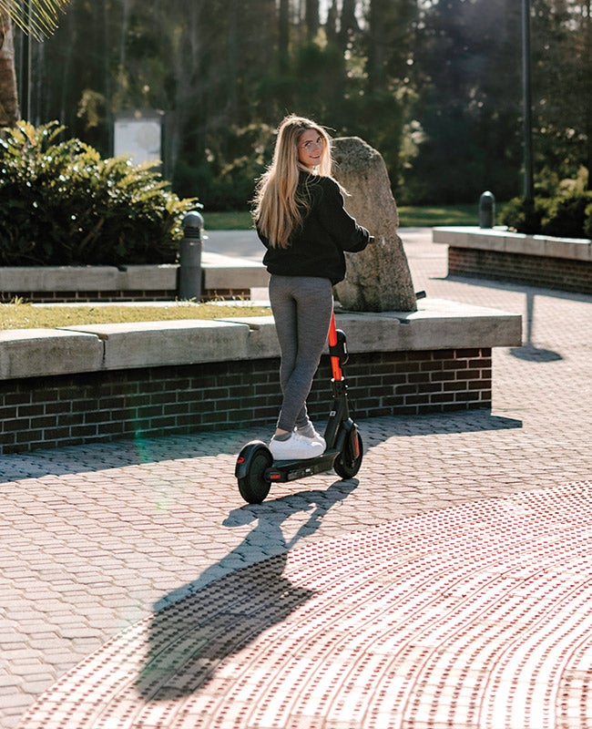 Woman rides a scooter on brick pavement