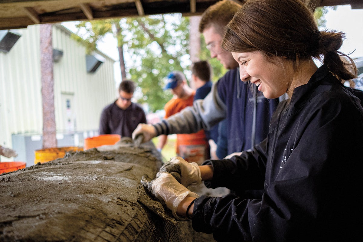 Two students sand a canoe in a workshop