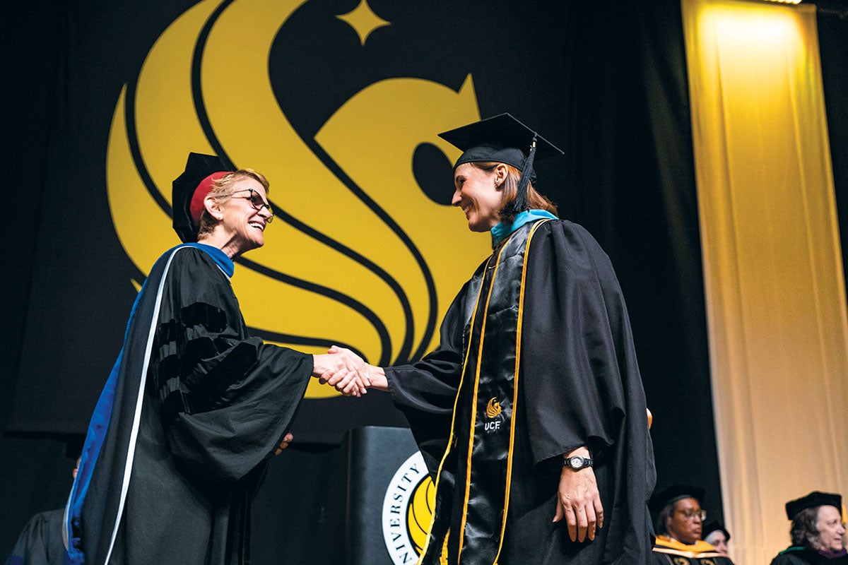 A graduate shakes someone's hand as she crosses the stage.