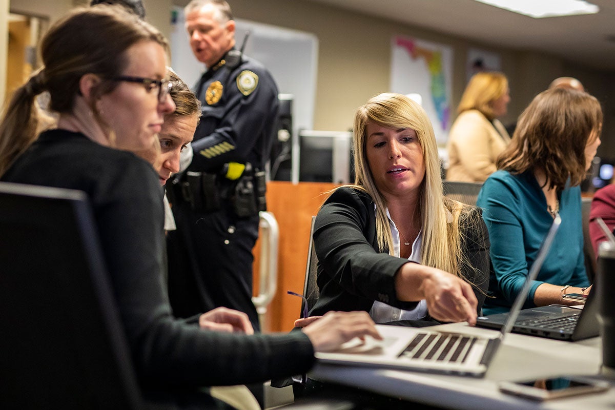 A woman points to a laptop screen while two women look at the screen.