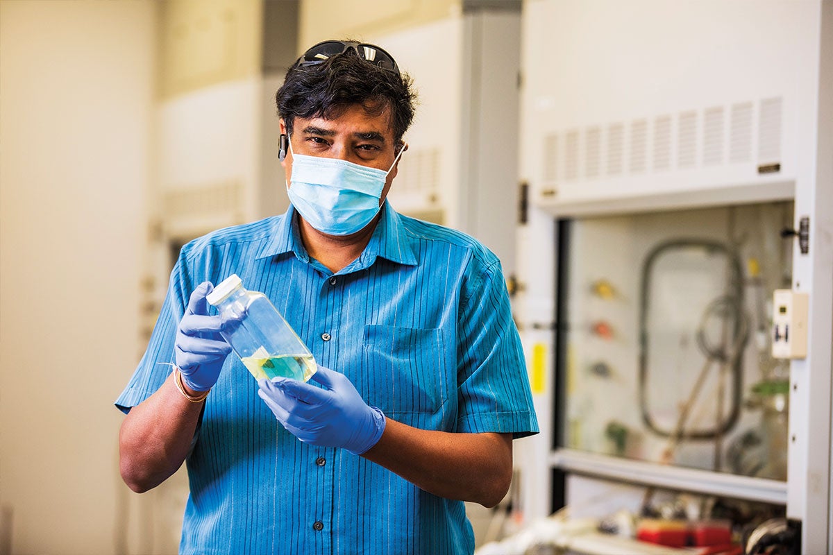 Sudipta Seal wears a mask while holding a bottle of a nanoparticle coating in a lab.