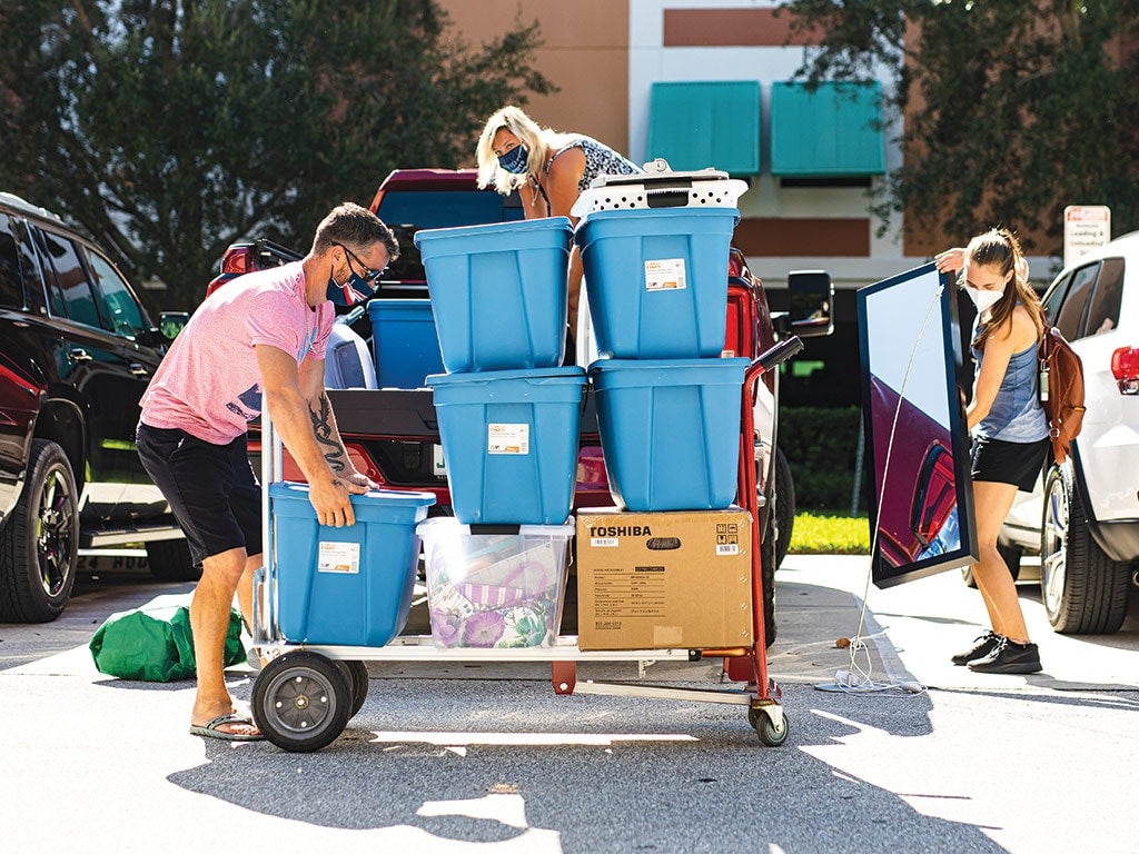 A student and two parents moving items into a dorm