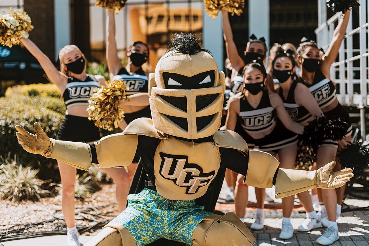 Knightro wears swim trunks while posing for a photo with UCF cheerleaders