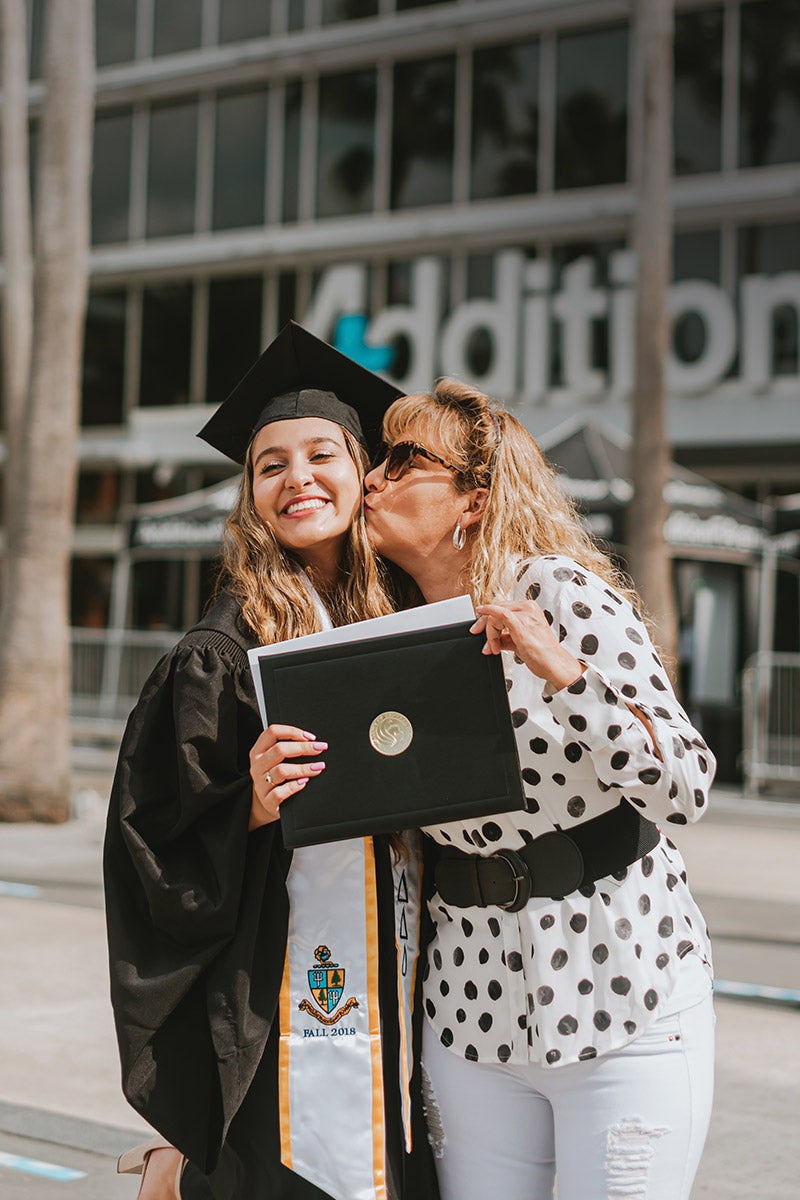 A Spring 2021 graduate poses for a photo with a family member in front of Addition Financial Arena.