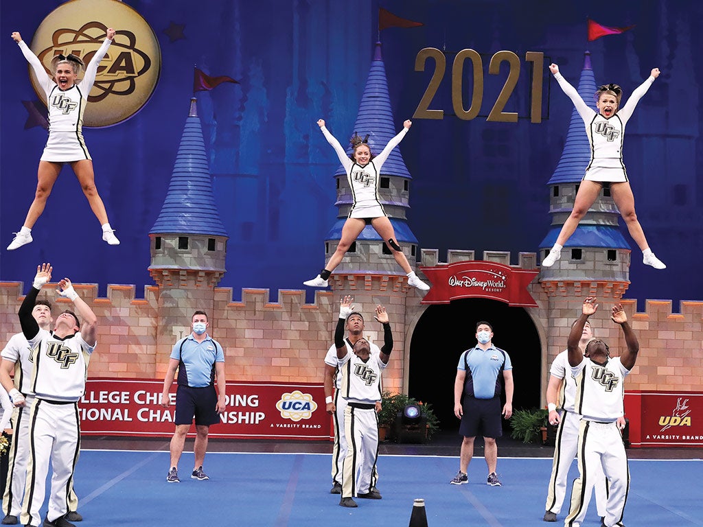 Cheerleading team during a performance, three flyers in the air as their spotters prepare to catch them