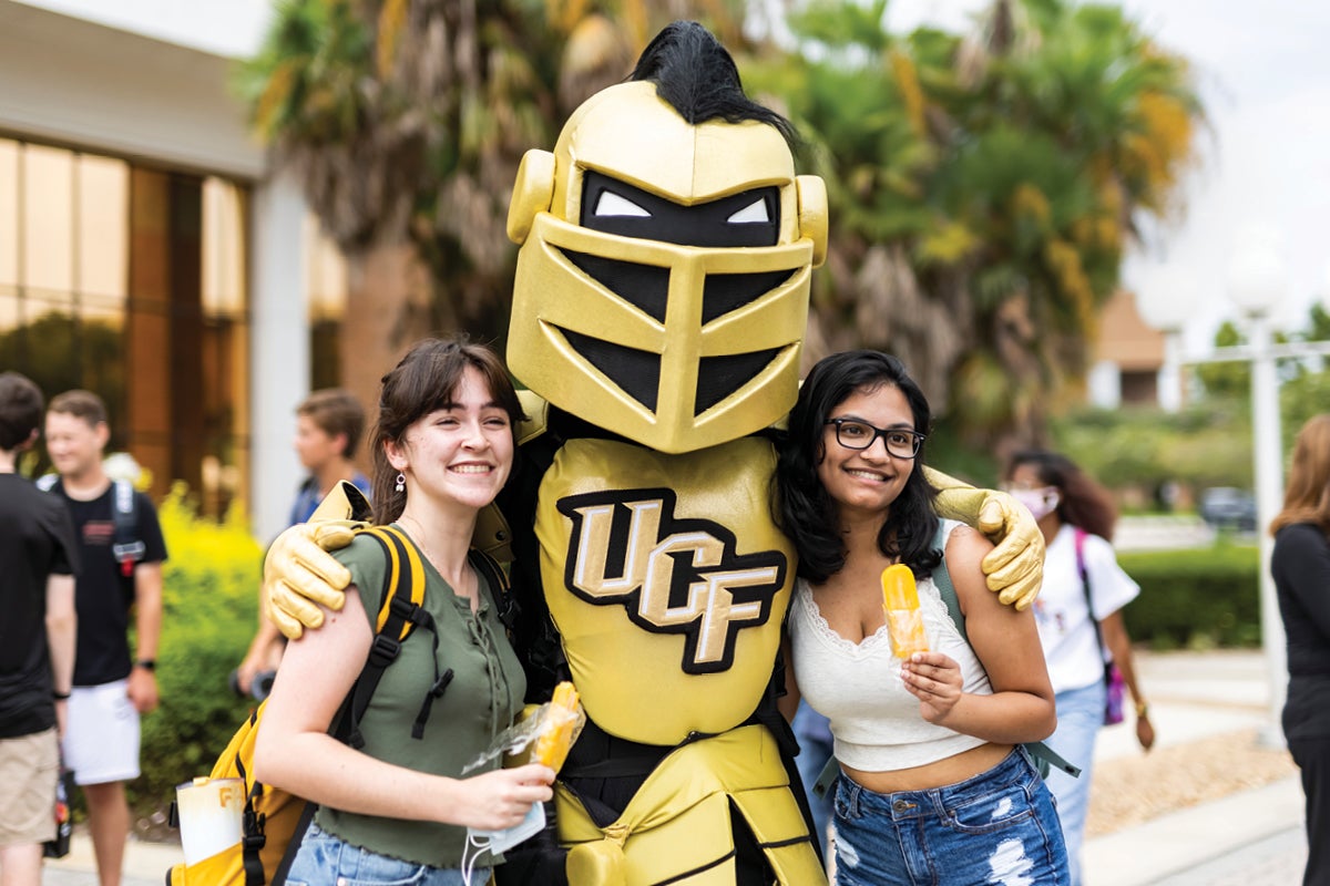 Two students hold popsicles while posing for a photo with Knightro