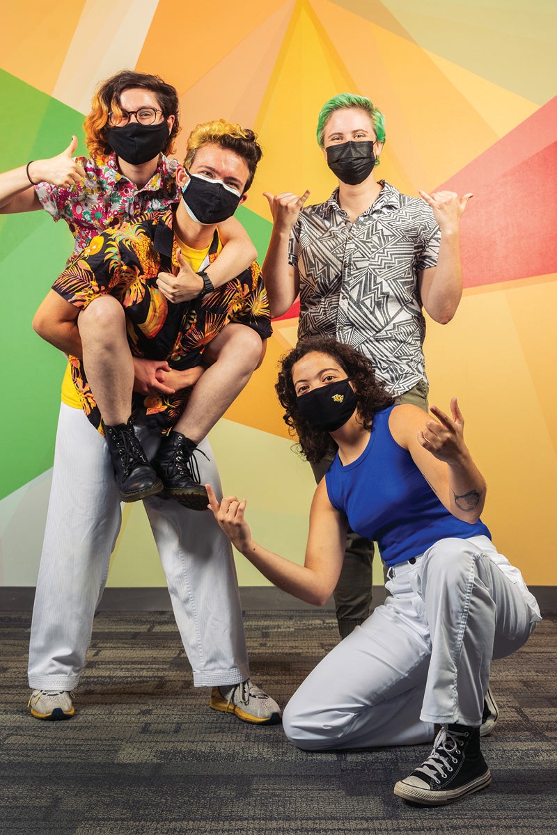 Four students pose for a photo in front of a colorful background