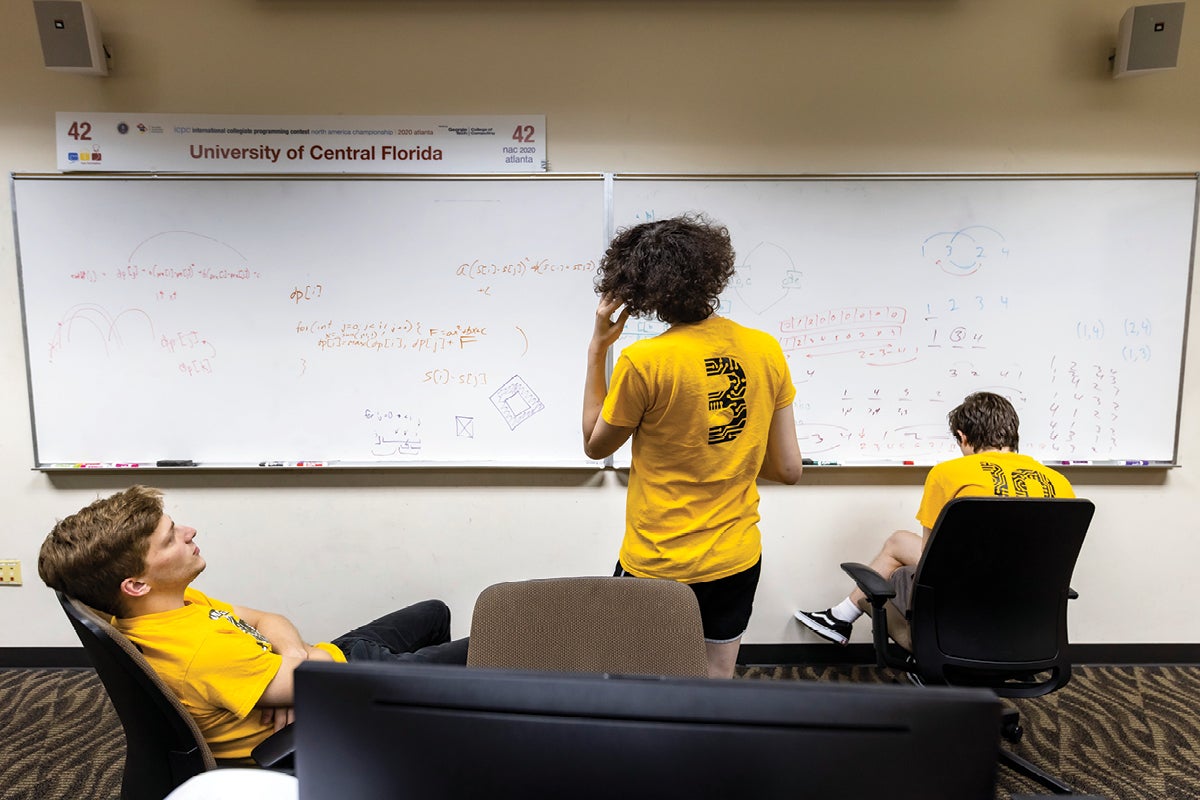 Three students stare at a whiteboard while trying to solve a computer programming issue