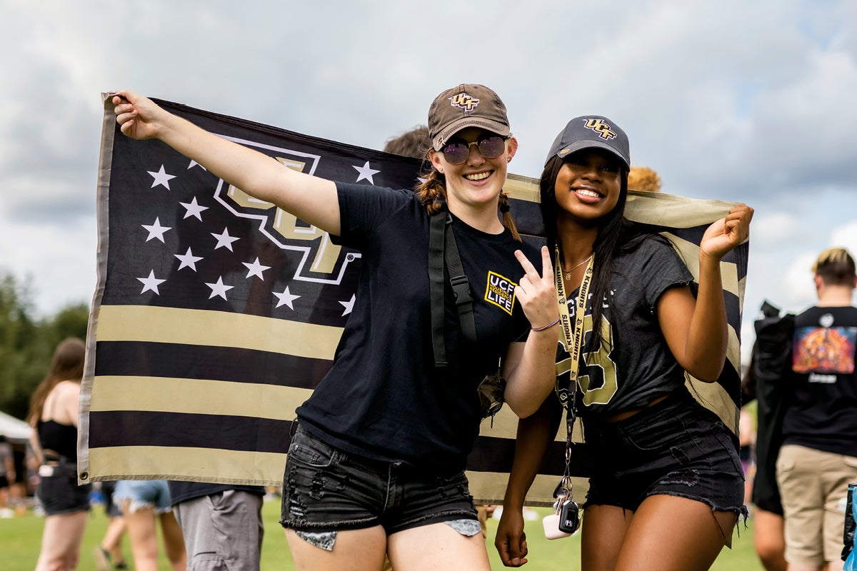 Two fans pose in front of a UCF flag