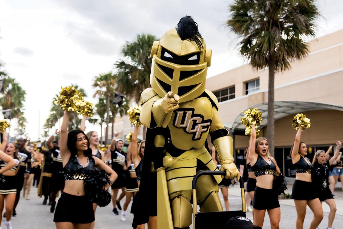 Knightro points at the camera while Knight Moves and the cheer team follow behind him during the March to Victory. Knightro points at the camera while Knight Moves and the cheer team follow behind him during the March to Victory.