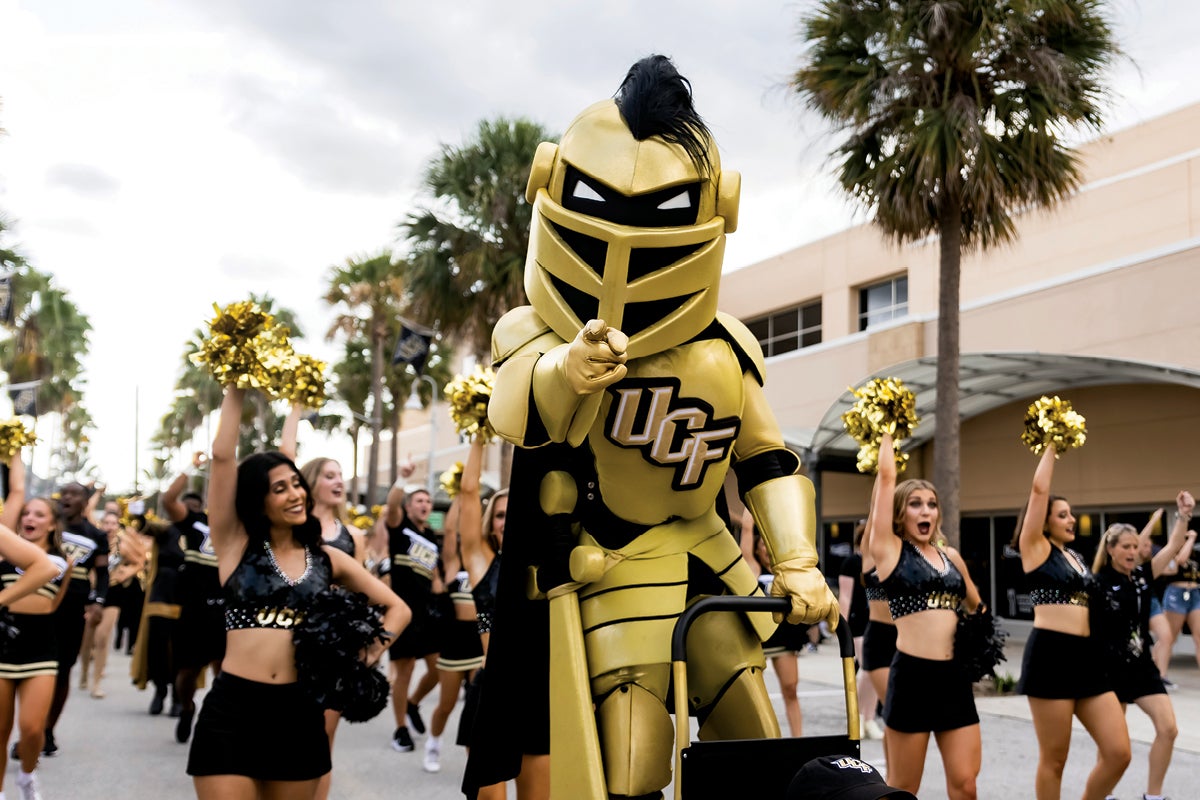 Knightro points at the camera while Knight Moves and the cheer team follow behind him during the March to Victory.