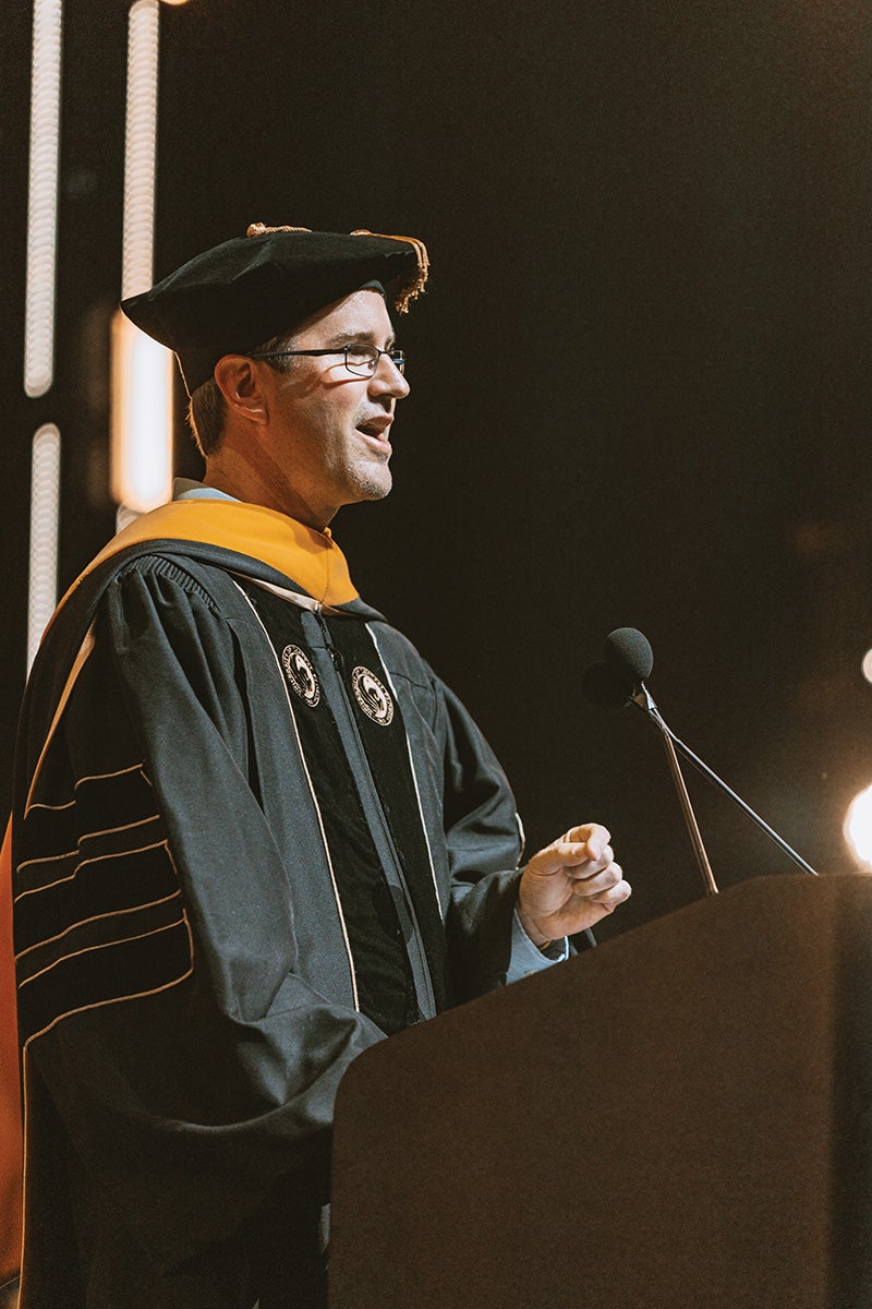 Darin Edwards wears a cap and gown while delivering a commencement speech.