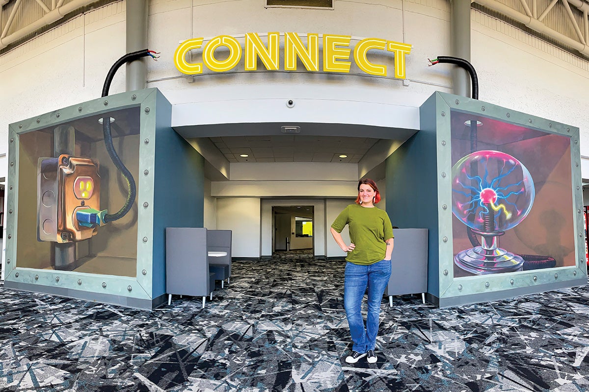 Naomi Haverland in front of a mural of a plug in a socket, plasma ball and the word 