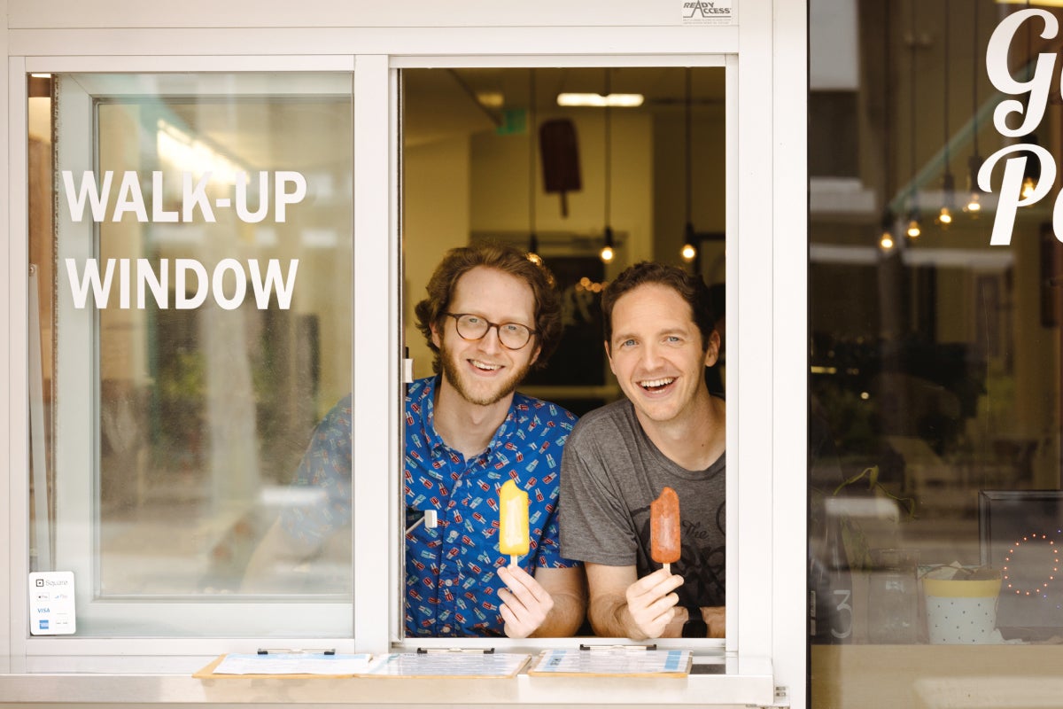 Adam and Brandon Chandler holding popsicles while smiling through their walk-up window.