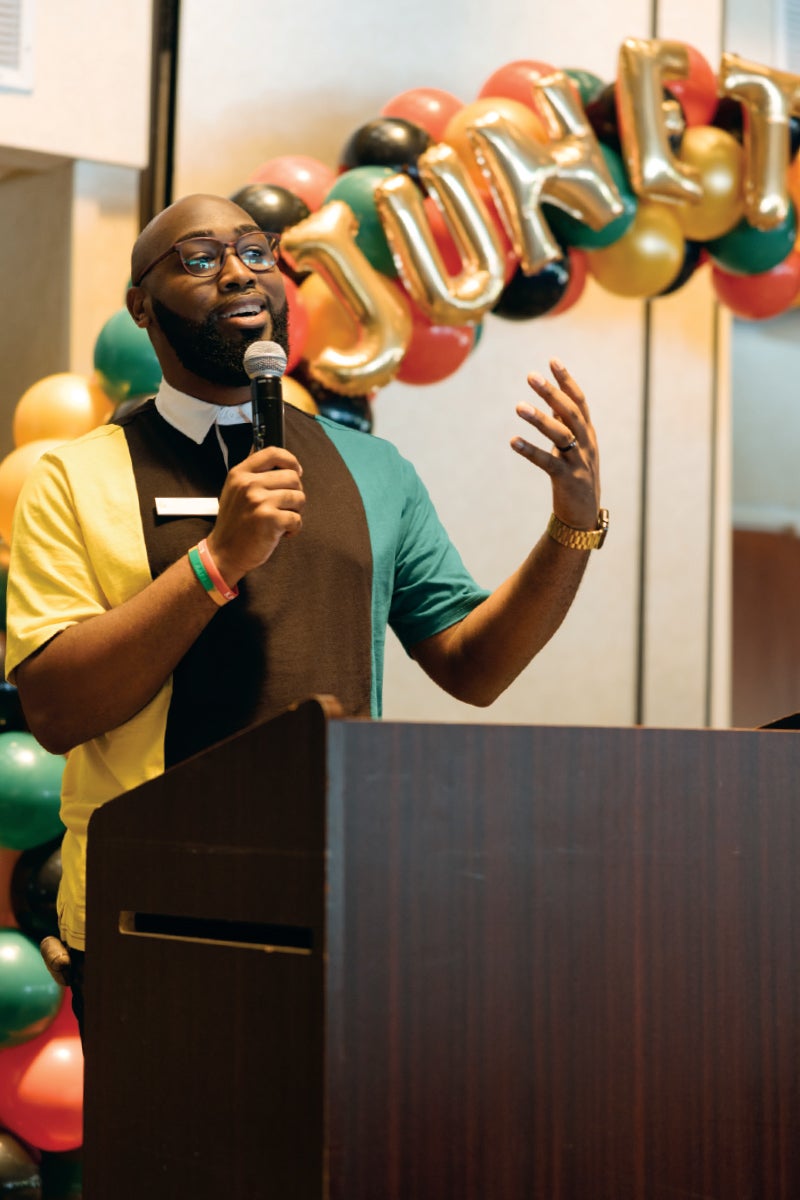 A man holds a mic and speaks at a podium with a 