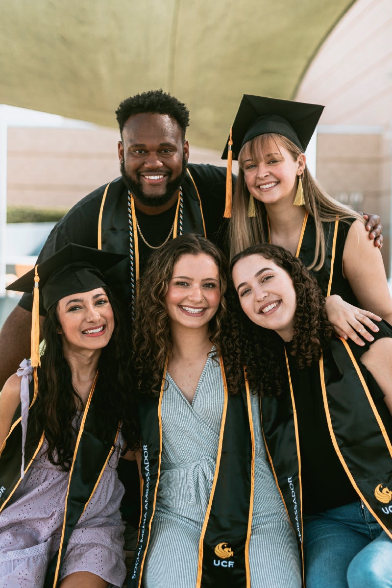 A group of ambassadors wearing graduation gaps, cords and tassels pose for a photo.