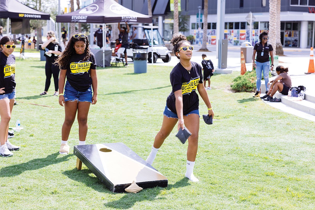 Three girls play cornhole on a lawn