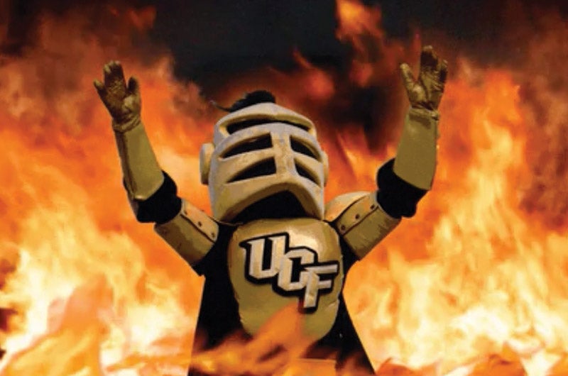 Knightro with his arms up and flames behind him