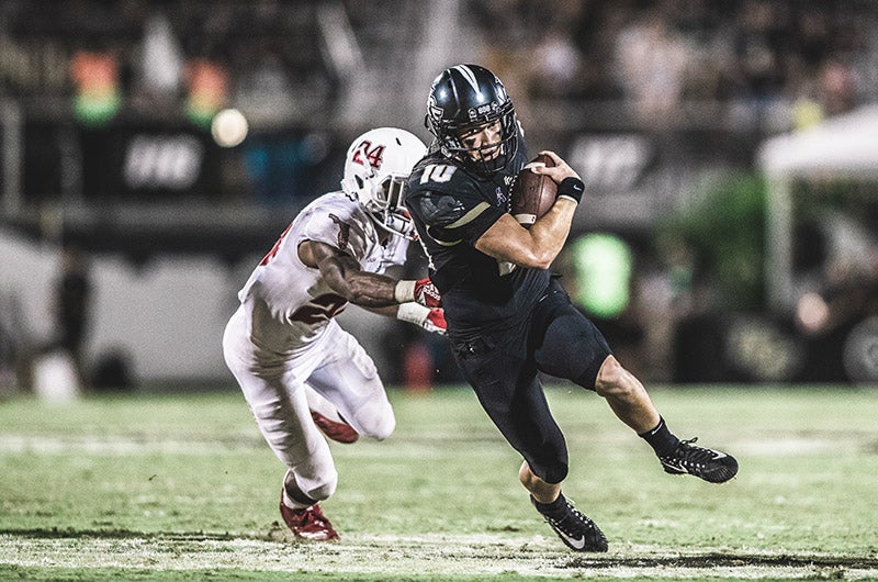 A football player holding a ball and running from a player on the opposing team.