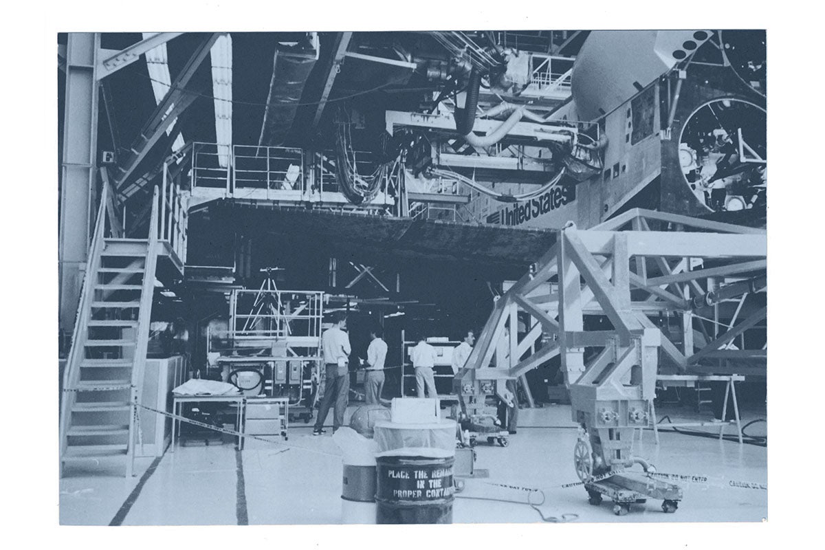 A black and white photo of a workspace under a space shuttle