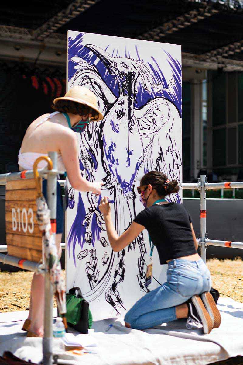 Two women fill in their canvas drawing of a bird with purple marker during UCF Celebrates the Arts' Creative Clash
