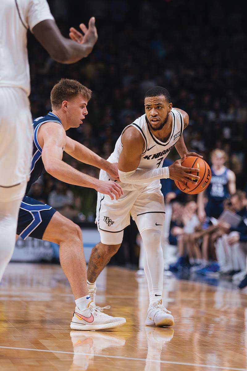 UCF men's basketball guard Darius Johnson holds the basketball away from a BYU defender.