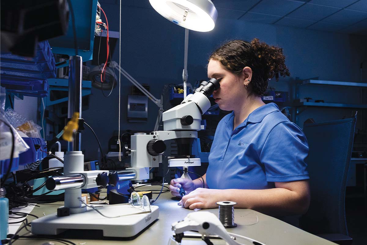 Lena Stadler looks into a microscope as she assembles a circuit board