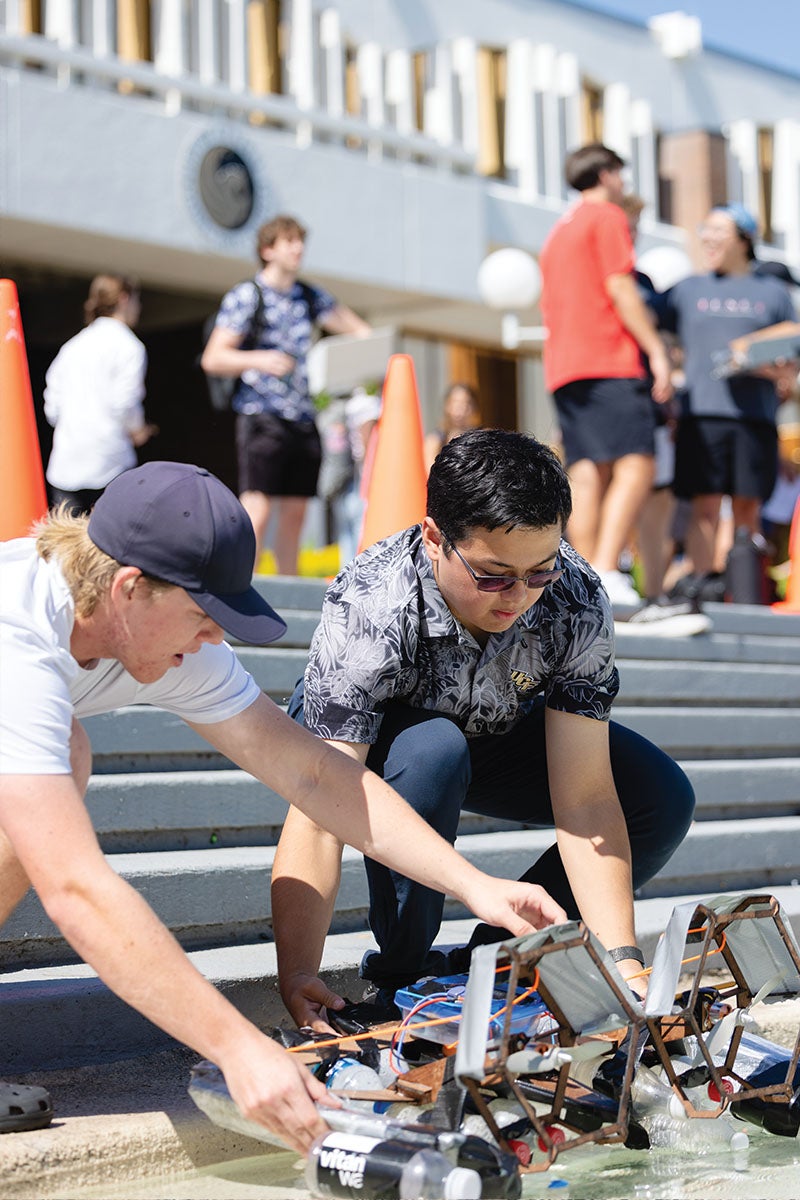 Two UCF engineering students kneel down to release their self-propelled boats into the Reflecting Pond during the Great Navel Orange Race.