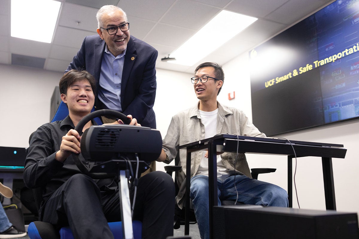 UCF professor Mohamed Abdel-Aty stands over two students operating a driver safety system in the UCF Smart and Safe Transportation Lab.