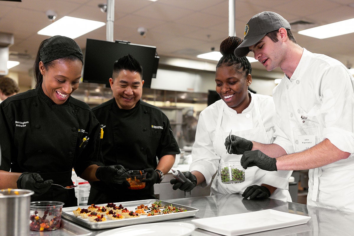 Two UCF students work with two instructor chefs to make gourmet appetizers in a culinary class at UCF's Rosen College of Hospitality Management.