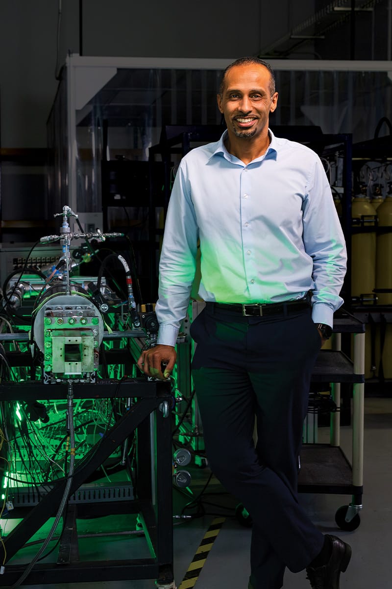 Trustee Chair Professor of Mechanical and Aerospace Engineering Kareem Ahmed stands beside a propulsion device, surrounded by wiring and equipment used for hypersonic research at the UCF HyperSpace Center.